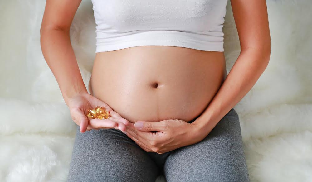 a pregnant woman with bare belly holding fish oil capsules.