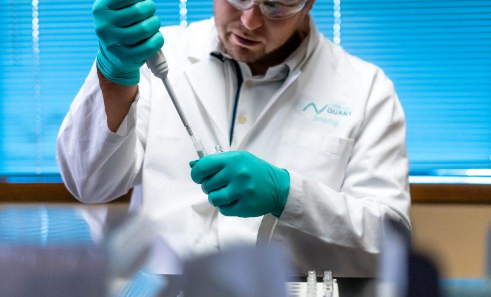 Laboratory technician wearing gloves and a lab coat using a pipette to transfer liquid into a test tube, conducting scientific analysis at OmegaQuant.