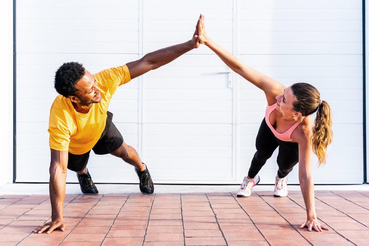 Fit couple doing a high-five while holding a plank position during an outdoor workout, symbolizing teamwork, fitness, and a healthy lifestyle.