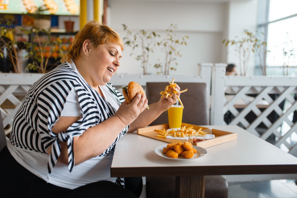 Overweight woman enjoying fast food meal with burger, fries, nuggets, and soda at restaurant — concept of unhealthy eating and high-calorie diet