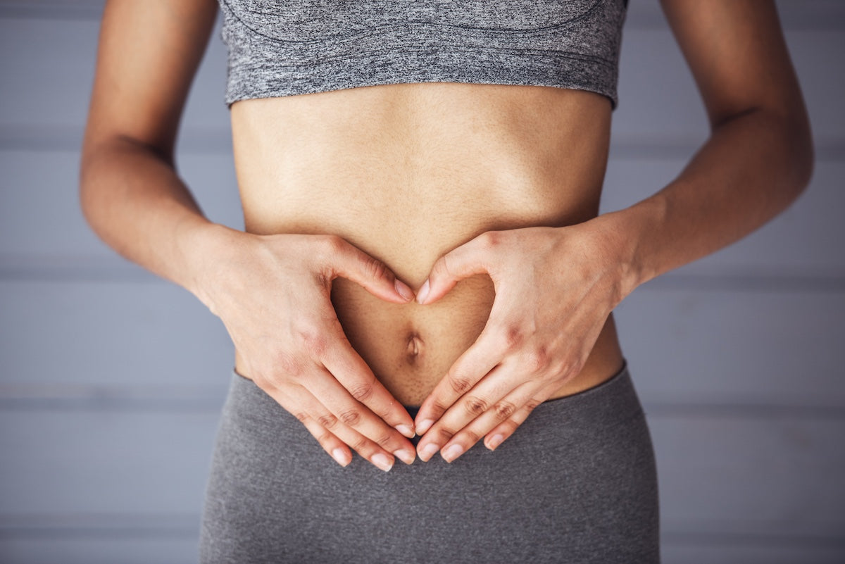 Close-up of a woman in athletic wear forming a heart shape with her hands over her stomach, symbolizing gut health and wellness.