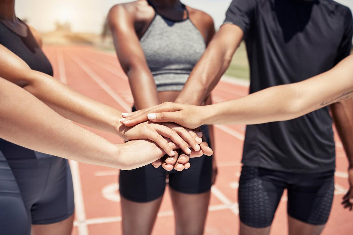 A group of athletes standing on a track with their hands stacked together in a show of teamwork and unity.
