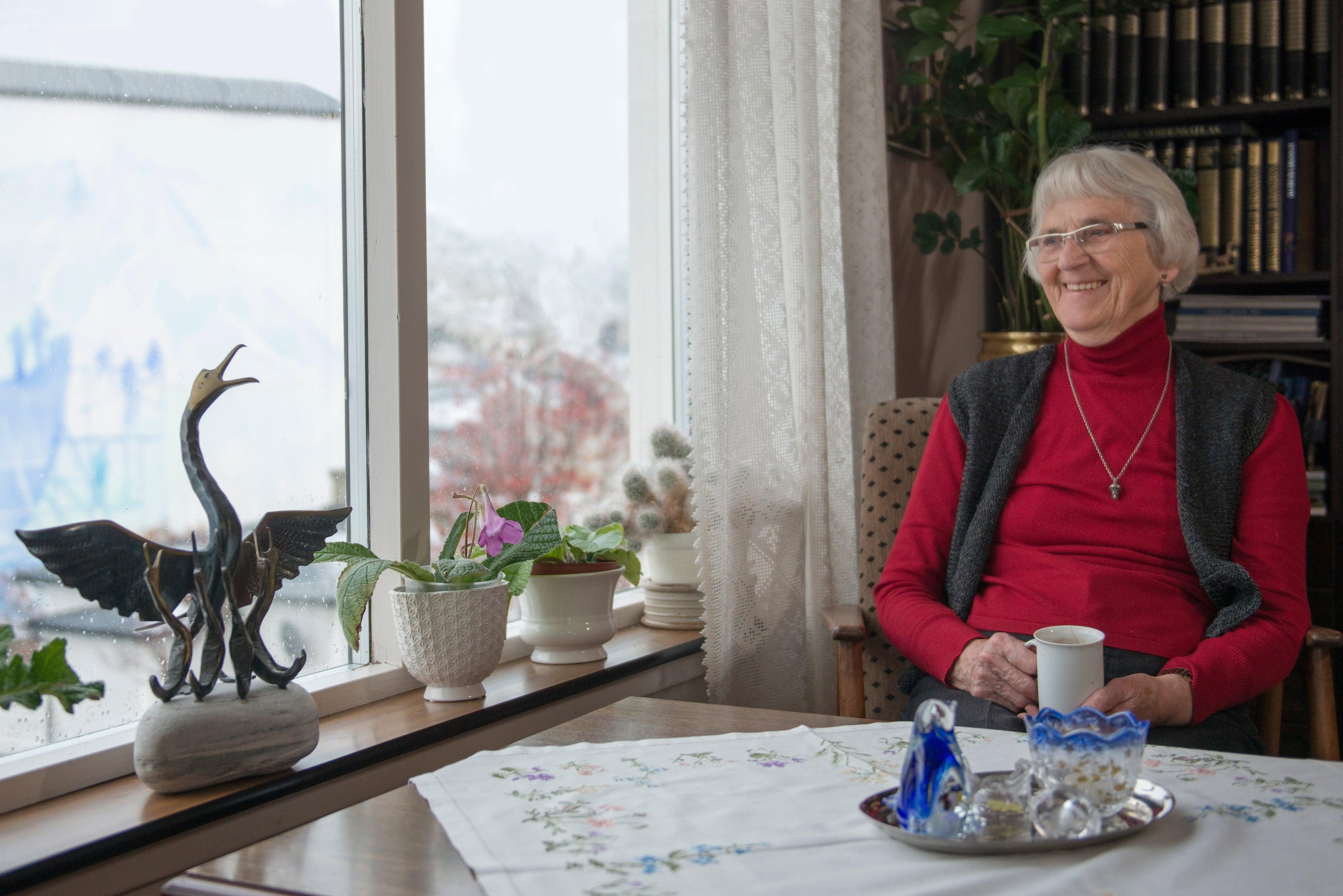 Malfrid Olsen sittin at her chair next to the window and drinking a hot beverage.