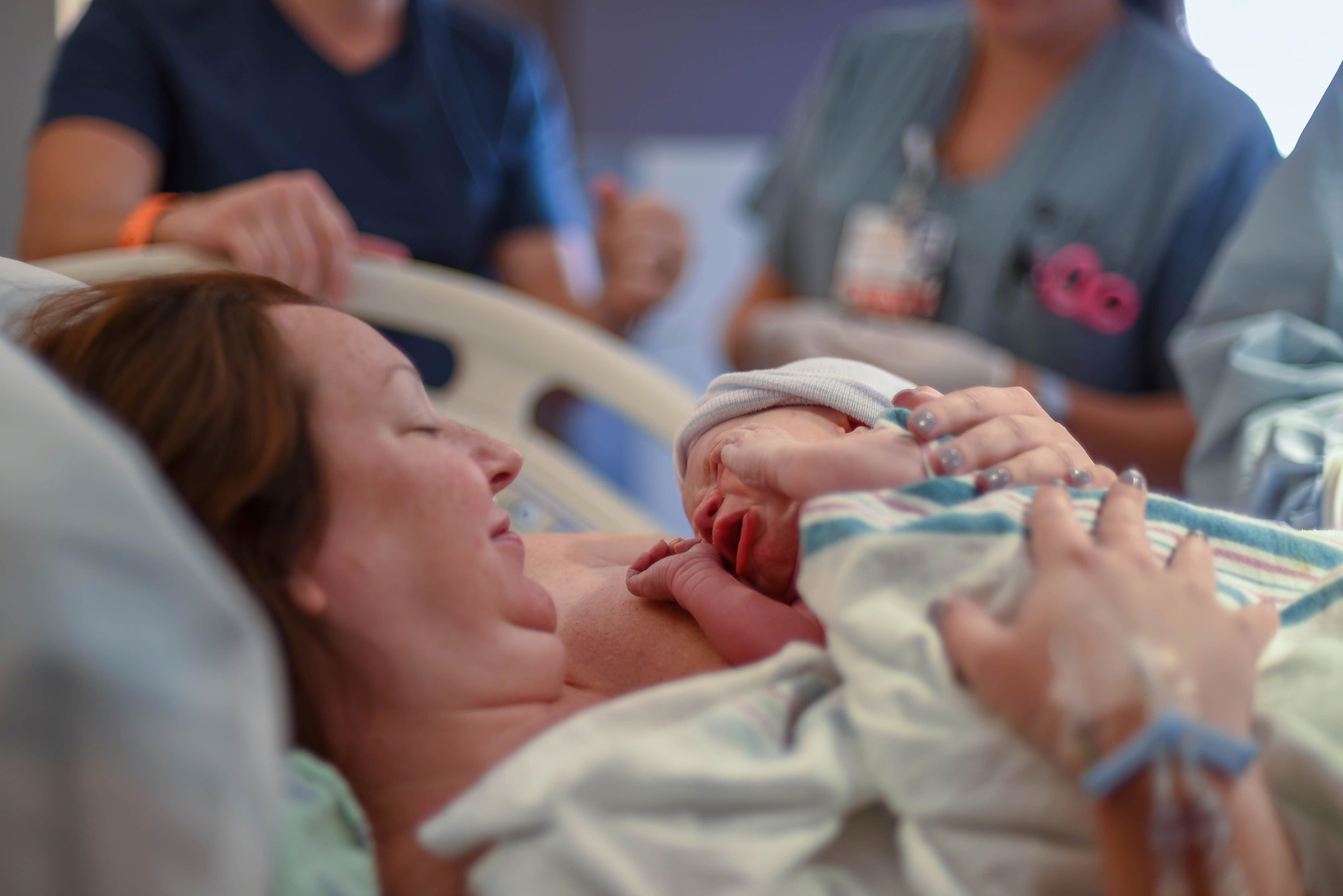 New mother holding her newborn baby for the first time in a hospital bed, surrounded by medical staff, showcasing the intimate and emotional moment of childbirth