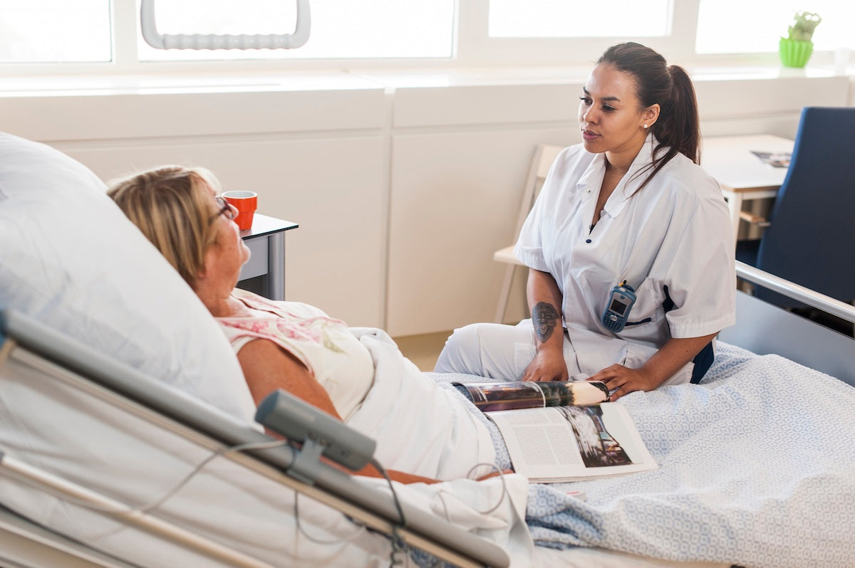 Nurse providing compassionate care to elderly female patient in hospital bed — healthcare support, patient recovery, and clinical caregiving