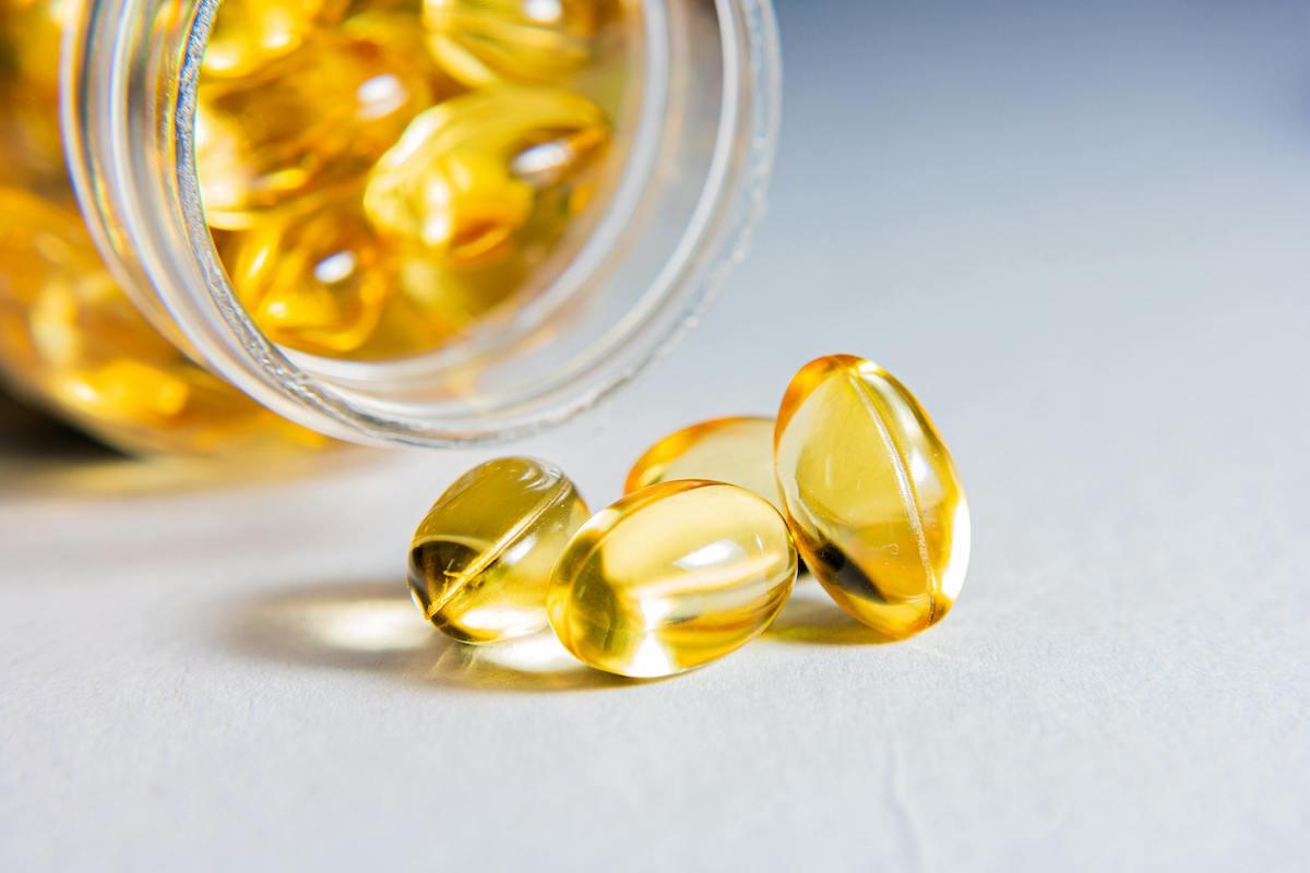 Close-up of transparent golden fish oil capsules spilling out of a glass jar onto a light surface.