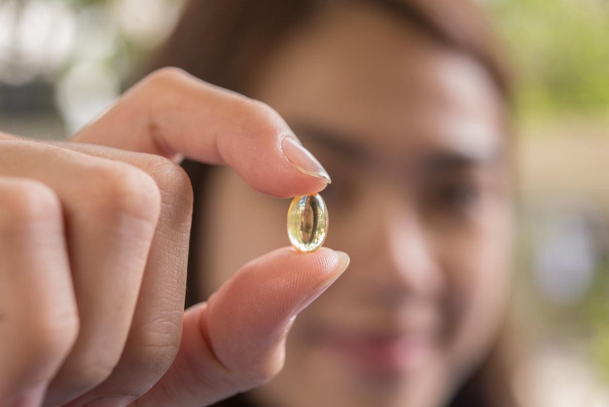 Woman holding a fish oil capsule between her fingers, highlighting the importance of omega-3 supplementation for health.