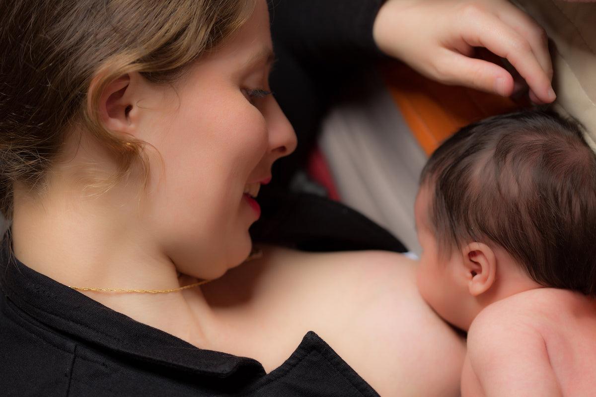 A young mother smiles lovingly while breastfeeding her newborn baby, showcasing the intimate bond and natural nourishment provided during nursing