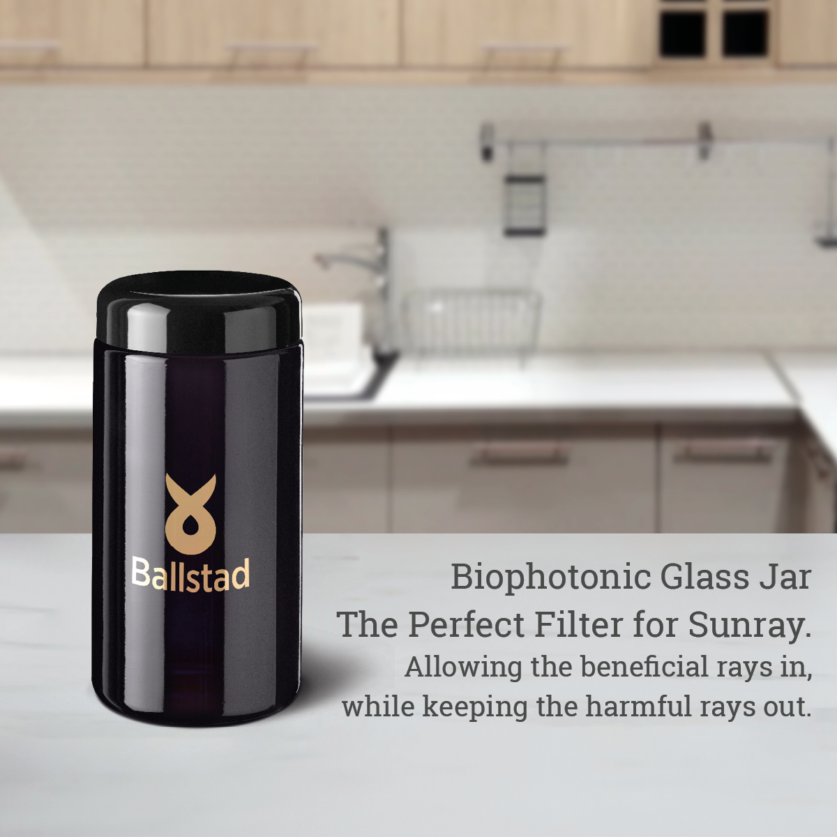 A dark violet Biophotonic glass jar labeled "Ballstad" is placed on a white kitchen countertop. The background features a modern kitchen with white cabinets and a dish rack. Text beside the jar reads: "Biophotonic Glass Jar - The Perfect Filter for Sunray. Allowing the beneficial rays in, while keeping the harmful rays out."