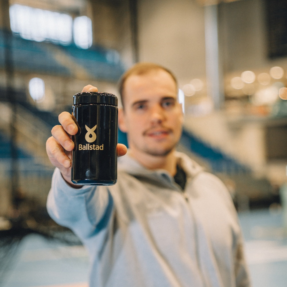 Athlete holding Ballstad Omega-3 supplement jar in sports arena — promoting performance nutrition and recovery support for active lifestyles