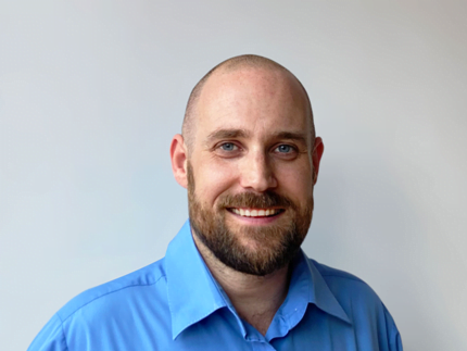 Odd Roar Olsen smiling with a blue shirt on in front of a gray solid background