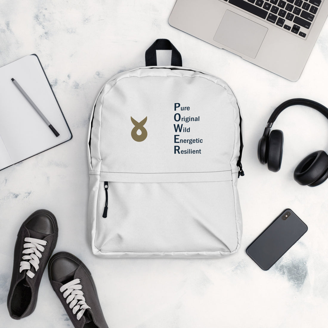 White backpack with the Ballstad logo and the acronym "POWER" (Pure, Original, Wild, Energetic, Resilient) displayed on a white surface, surrounded by black sneakers, a smartphone, wireless headphones, an open notebook with a pen, and a silver laptop.