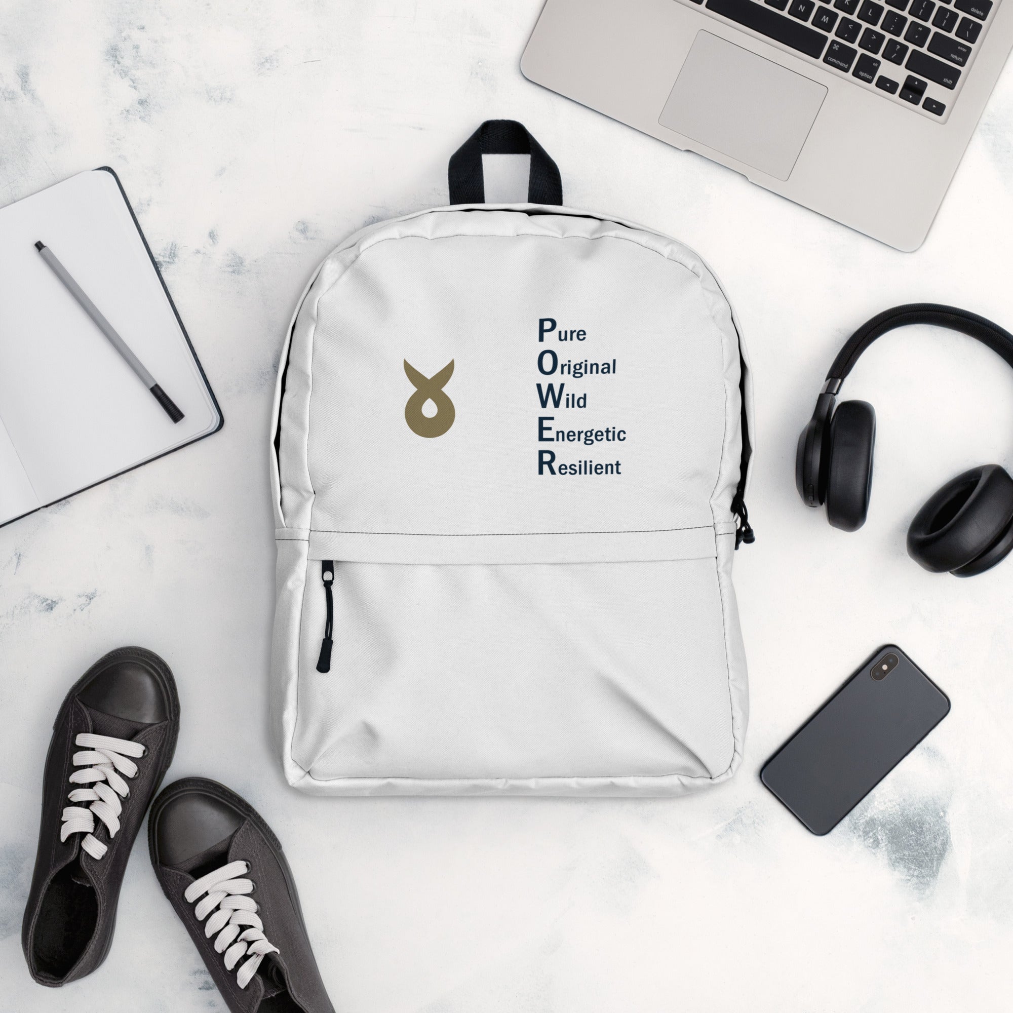 White backpack with the Ballstad logo and the acronym "POWER" (Pure, Original, Wild, Energetic, Resilient) displayed on a white surface, surrounded by black sneakers, a smartphone, wireless headphones, an open notebook with a pen, and a silver laptop.