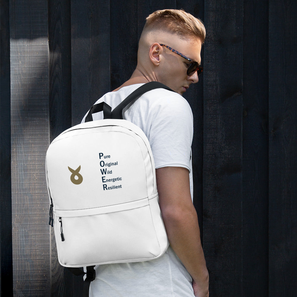 Young man wearing sunglasses and a white t-shirt stands against a dark wooden wall, carrying a white backpack with the Ballstad logo and the acronym "POWER" vertically spelled out as Pure, Original, Wild, Energetic, Resilient.