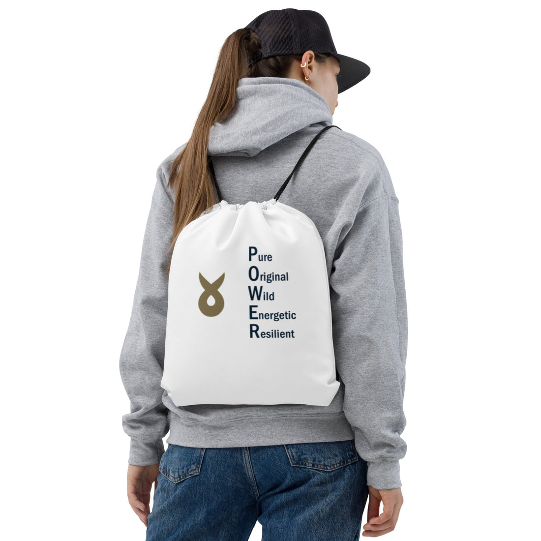 Woman wearing a gray hoodie and black cap, carrying a white drawstring backpack printed with the word "POWER" as a vertical acronym (Pure, Original, Wild, Energetic, Resilient) and a gold Ballstad logo beside the text.