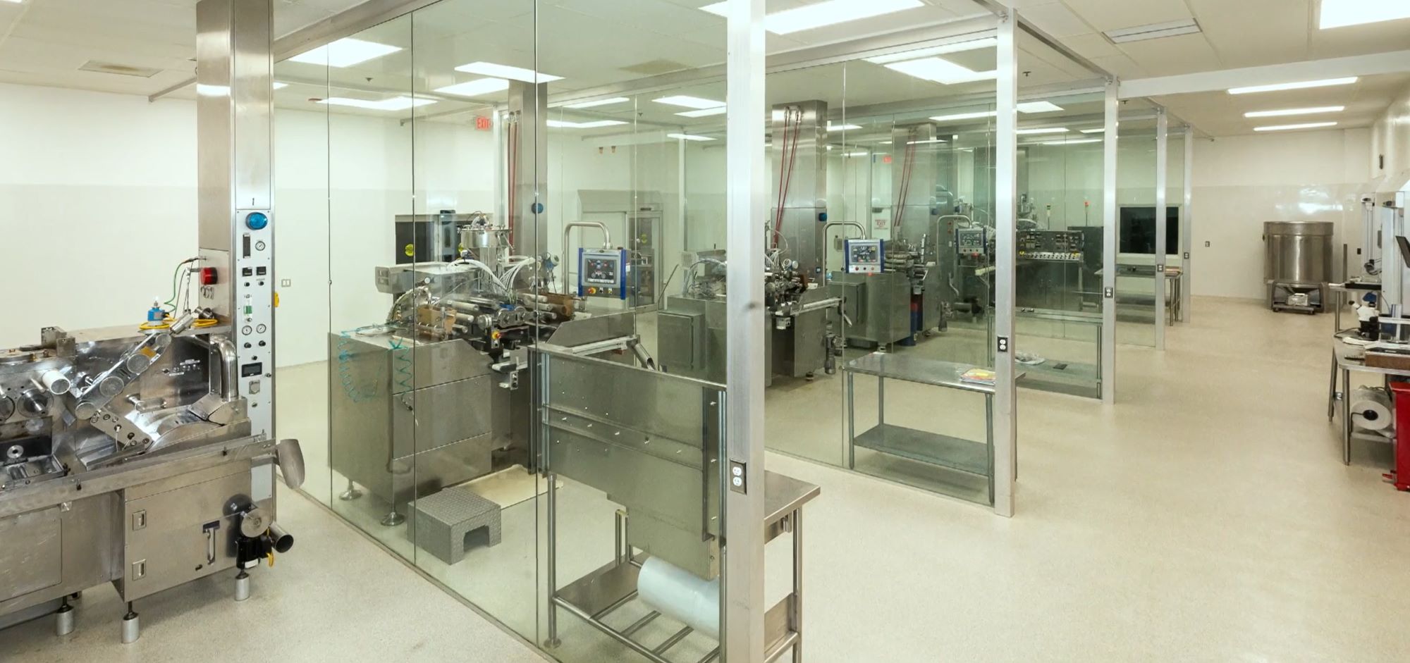 An industrial place with multiple steel machines side by side, separated with a glass window