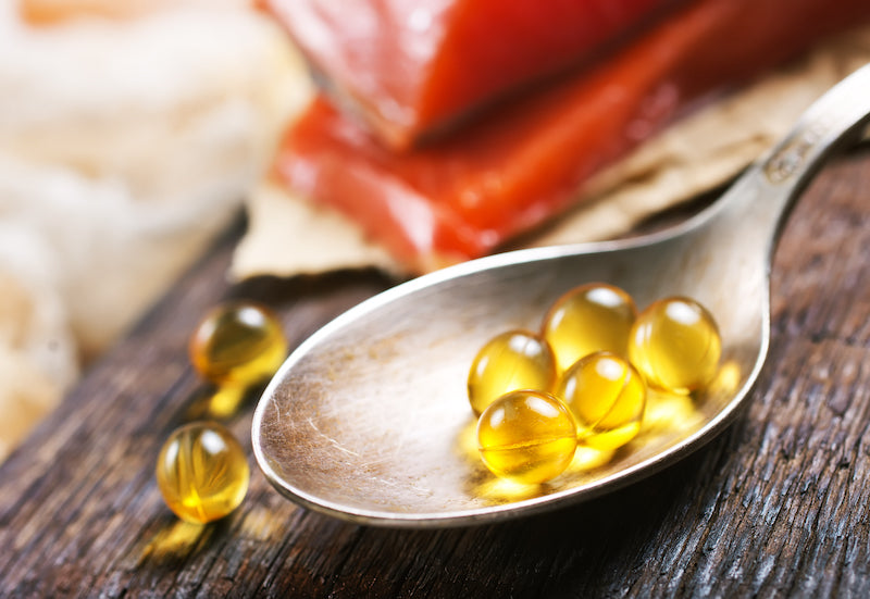 Fish oil capsules in a spoon on a wooden table with salmon fillets in the background