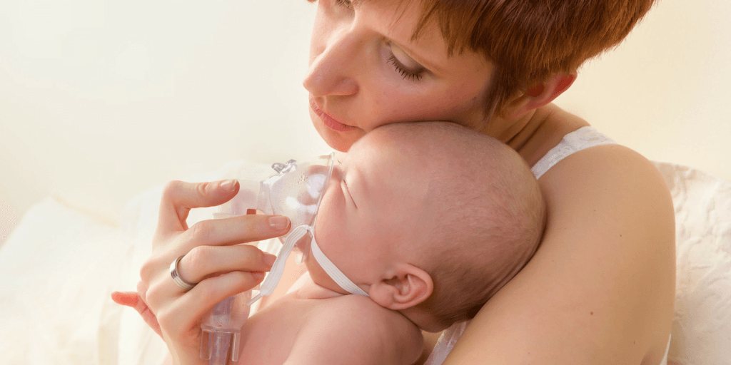 A mother gently holds her infant while administering a nebulizer treatment, highlighting concern and care during a respiratory episode, possibly related to asthma or breathing difficulties.