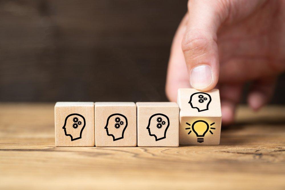 Hand placing wooden block with human head and light bulb icon — concept of innovation, cognitive development, and creative thinking