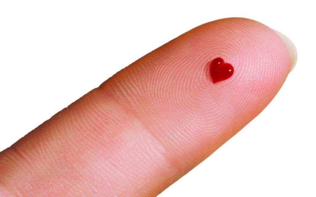 Close-up of a fingertip with a small drop of blood shaped like a heart, symbolizing health, wellness, and blood testing.