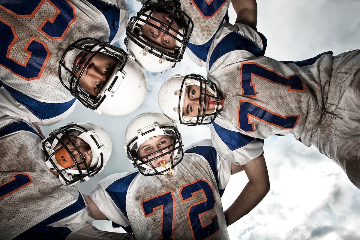 Youth football team in a huddle wearing helmets and jerseys — teamwork, motivation, and strategy in American football game