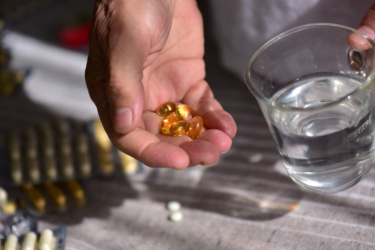A morning dose of medicine in the hand of an elderly man and a glass of water ready to be consumed