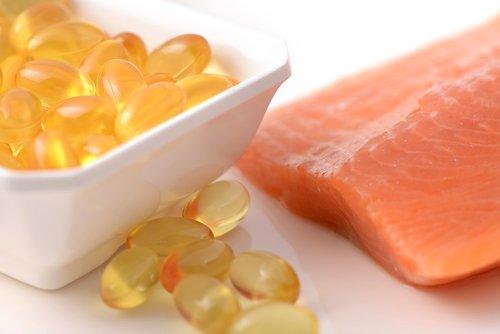 A close-up image of omega-3 fish oil capsules in a white dish next to a raw salmon fillet, symbolizing dietary sources of EPA and DHA.