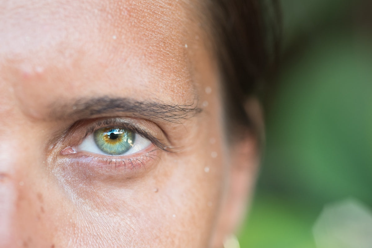 Close-up of a woman's green eye and facial skin, highlighting eye health and natural detail with a blurred green background.