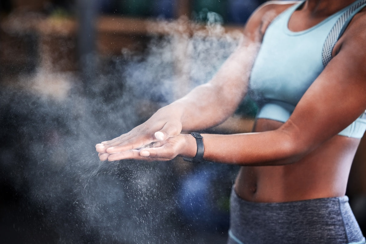 Close-up of a fit young woman in athletic wear clapping chalked hands at the gym, with chalk dust floating in the air.
