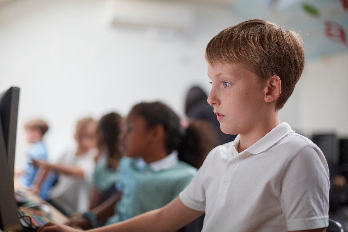 Blonde boy focused and engaged in computer in the class with peers