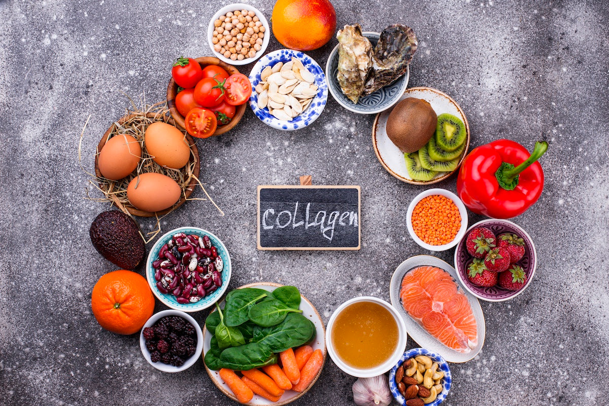 Assortment of collagen-rich foods including salmon, eggs, beans, spinach, kiwi, citrus fruits, nuts, and bone broth, arranged around a chalkboard labeled ‘Collagen’.
