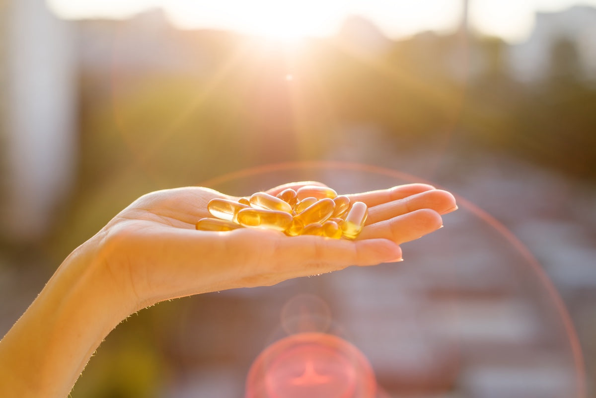 A hand holding several golden omega-3 fish oil capsules, with sunlight shining in the background, symbolizing health, supplementation, and natural wellness.