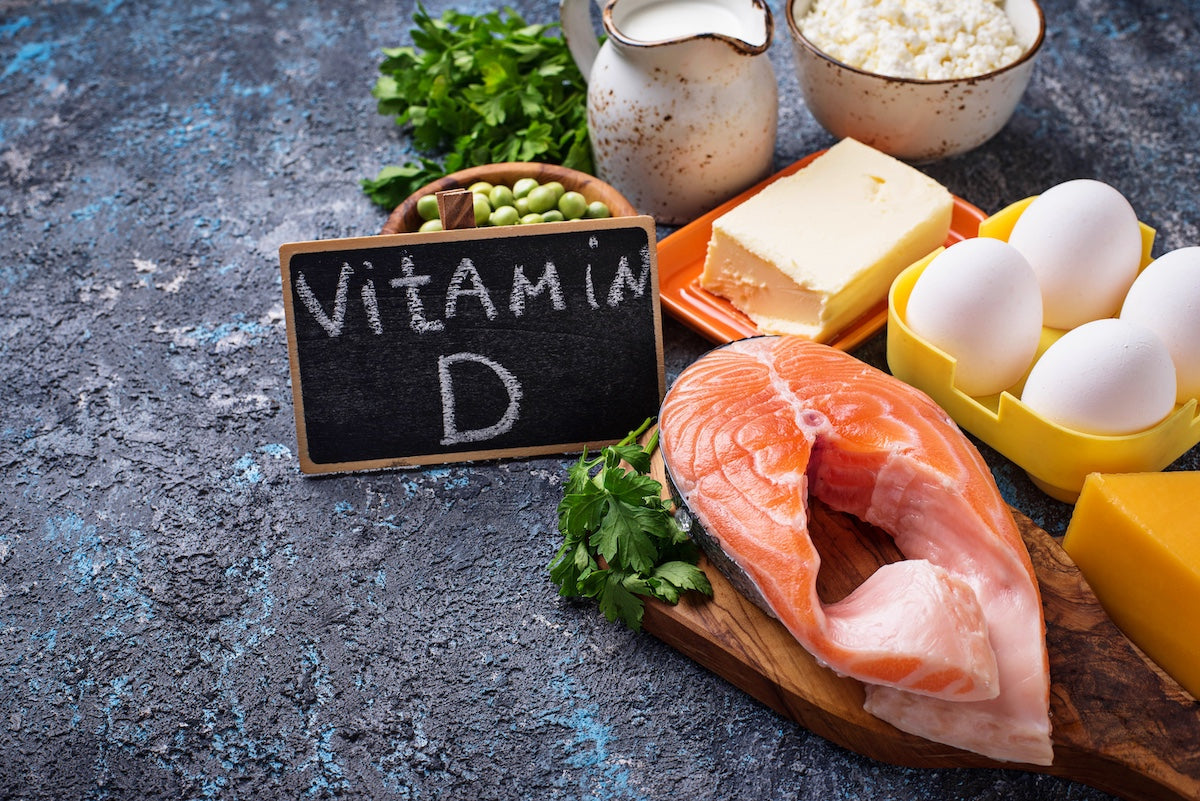 eggs, dairy, herbs, cheese and salmon on dark background with vitamin d written on a black board next to it. 