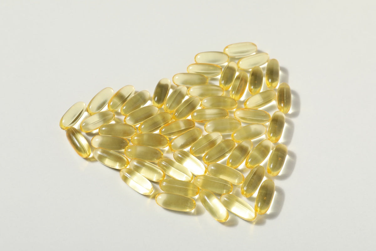 A group of yellow omega-3 fish oil capsules arranged in the shape of a heart on a white background, symbolizing heart health and cardiovascular support.