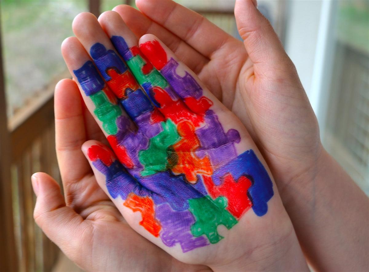A close-up of a child's hand painted with colorful puzzle pieces, symbolizing autism awareness, gently held by an adult's hand.