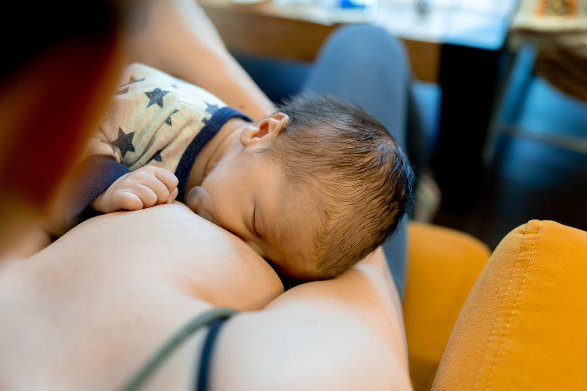 Close-up of a newborn baby breastfeeding, showing the baby’s head resting against the mother’s chest while feeding.