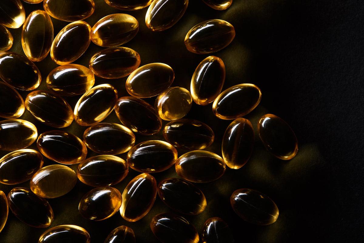 Close-up of shiny omega-3 fish oil capsules on a dark background.