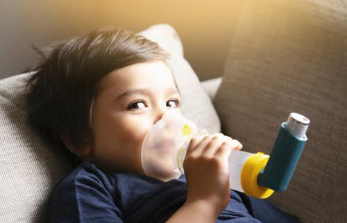 a child lying on the sofa inhaling his asthma medicine