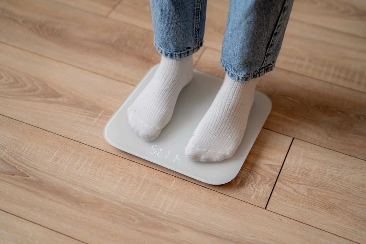 Person wearing white socks standing on a digital scale on a wooden floor, checking their weight.