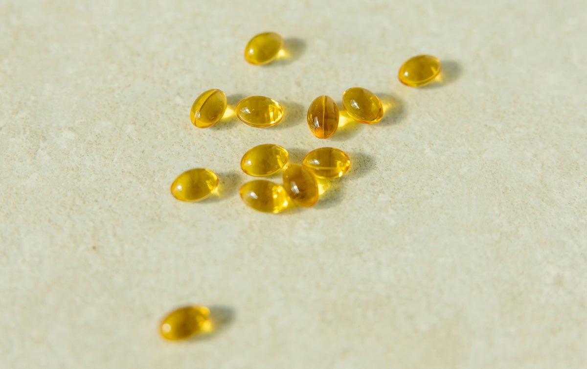 Golden omega-3 fish oil softgel capsules scattered on a beige surface, illustrating high-quality dietary supplement pills.