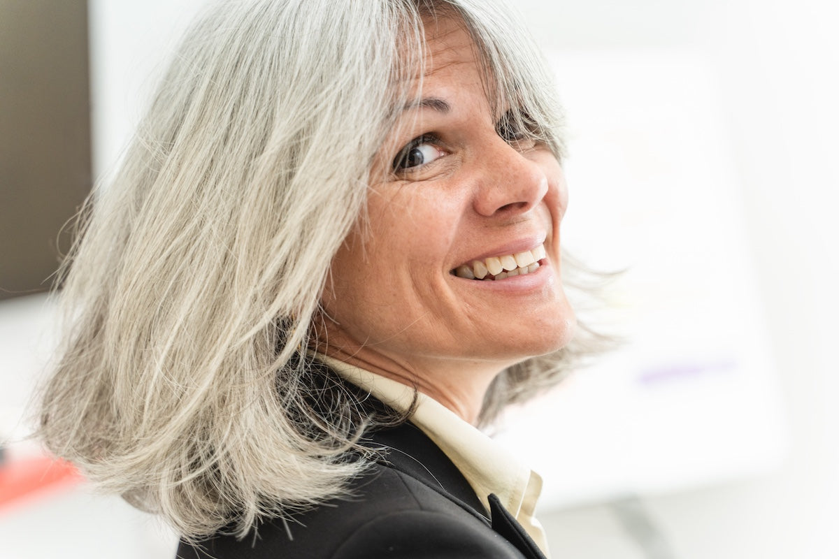 Smiling middle-aged woman with gray hair looking over her shoulder in a bright indoor setting