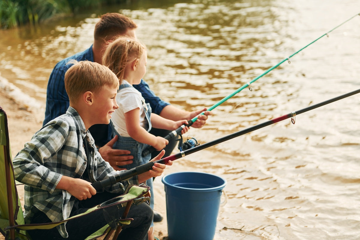 Sitting together. Father with son and daughter on fishing outdoors at summertime.