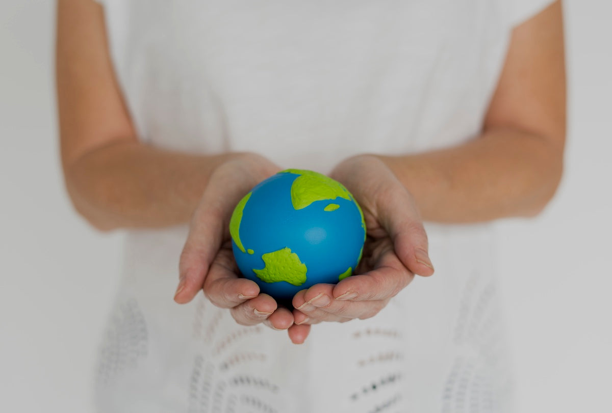 Person holding a small blue and green globe in their hands, symbolizing environmental care and sustainability.