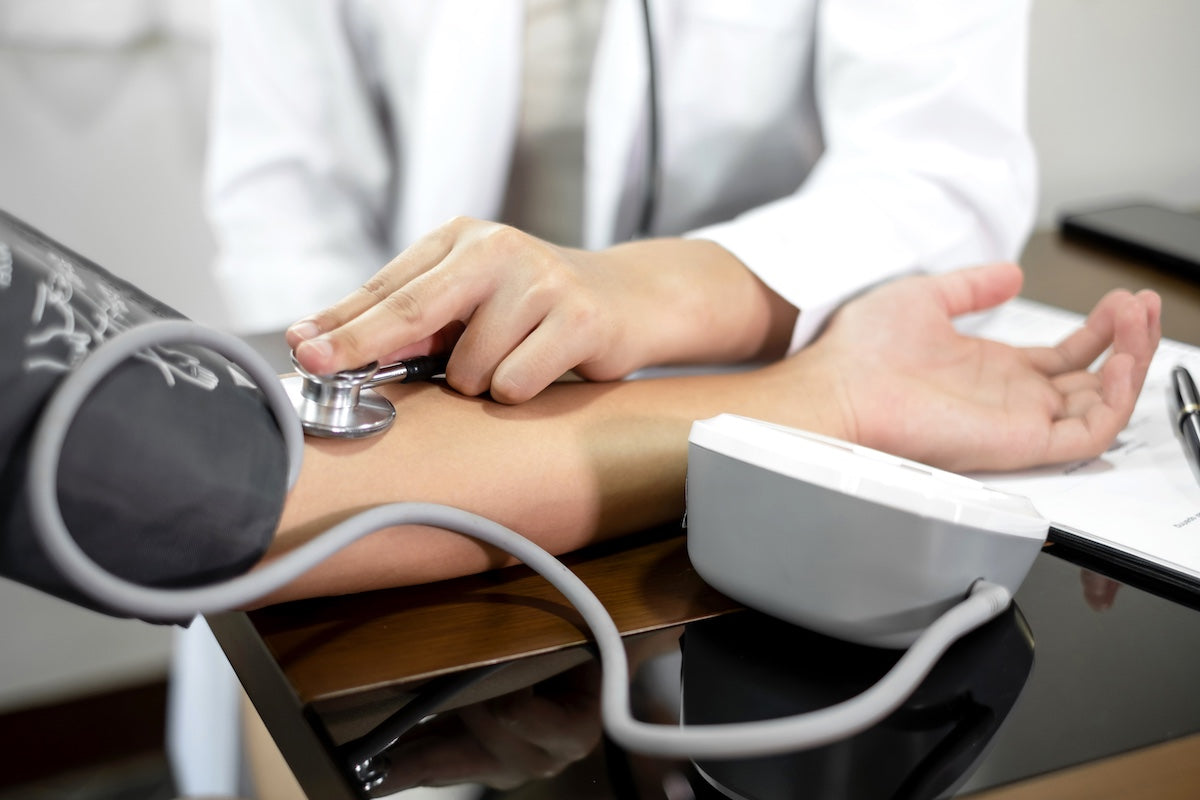 A healthcare professional using a stethoscope and blood pressure monitor to measure a patient’s blood pressure, representing routine cardiovascular health assessment.