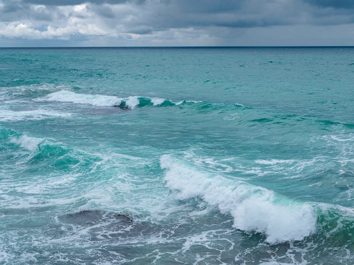 A scenic view of turquoise ocean waves crashing against a rocky shoreline under a cloudy sky, highlighting the power and beauty of marine environments.