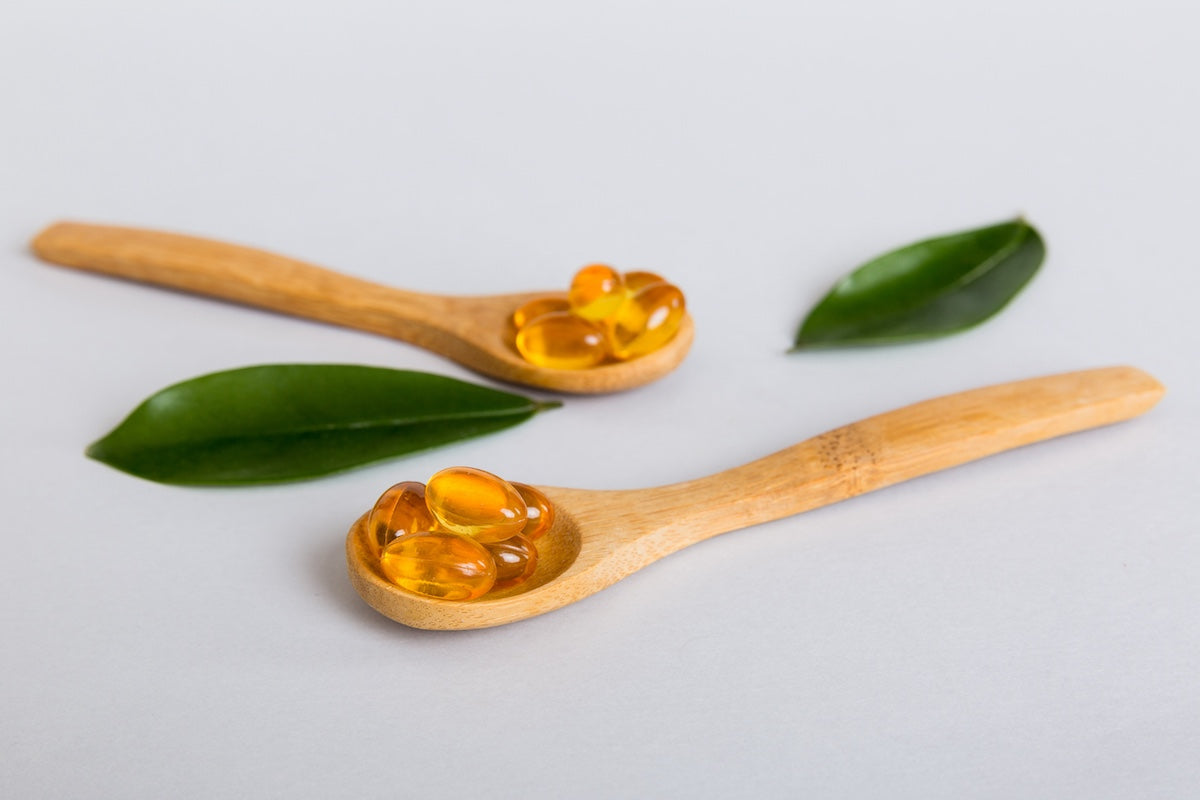 Vitamin omega-3 capsules in a spoon on a colored background. Pills served as a healthy meal. Red soft gel vitamin supplement capsules on spoon.