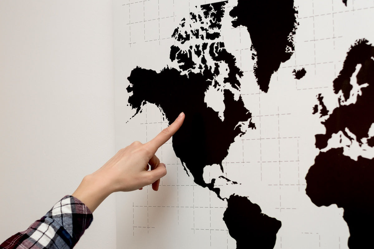 A person pointing to a location in North America on a black-and-white world map, highlighting geographic focus or regional interest.