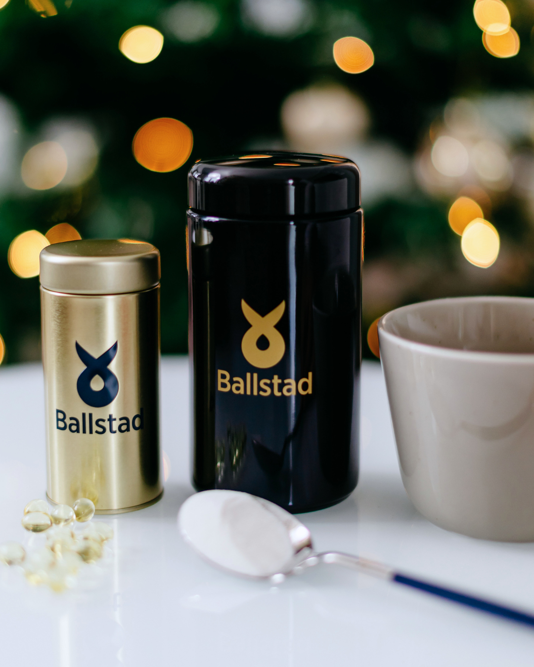 Two Ballstad containers, one gold and one black, on a white surface with a blurred Christmas tree in the background.