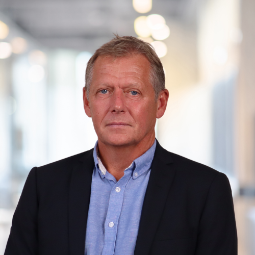 Terje Evensen portrait with a blue shirt and a blazer on, in a light coloured room