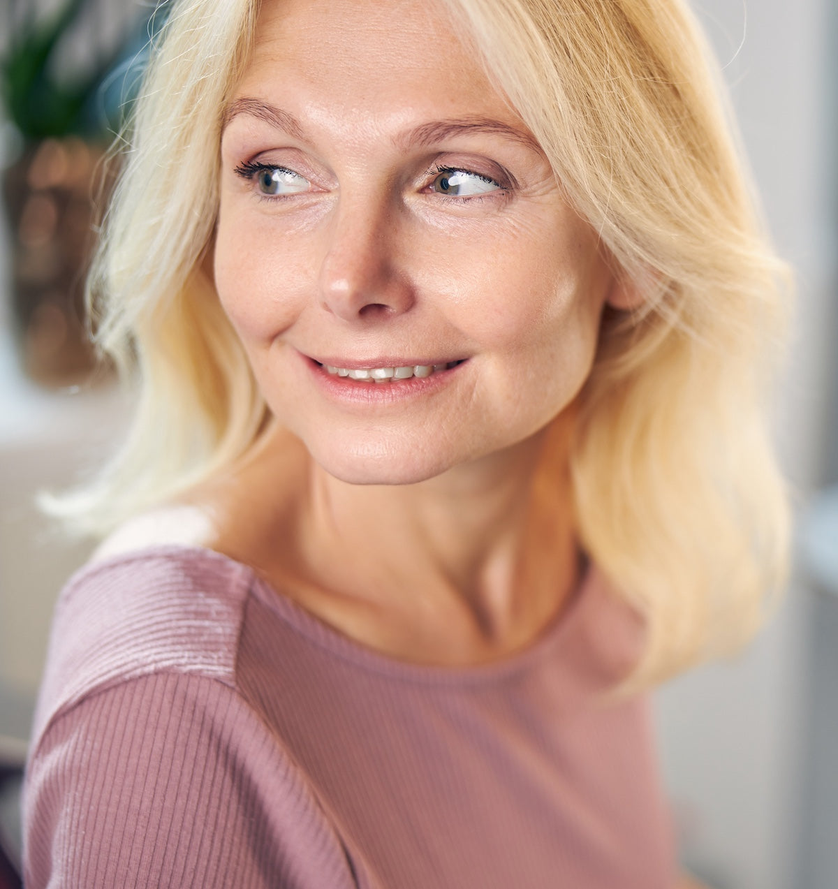 Woman with blonde hair wearing a pink sweater indoors